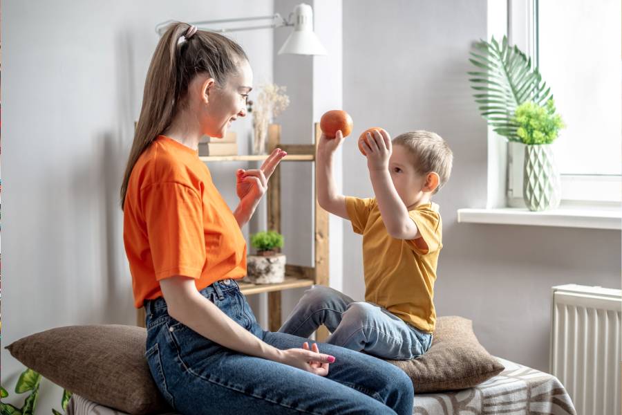 A happy mother in a playful way is teaching her little son to count using fruits.